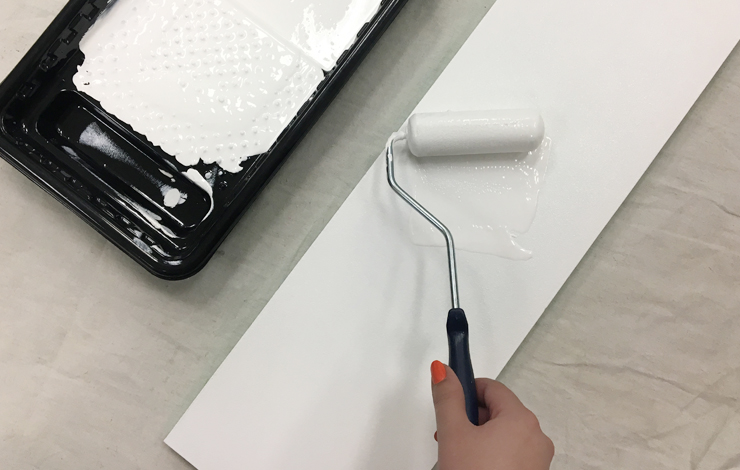 Paint tray and roller with white paint. A person is painting wood boards.
