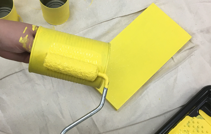Painting a can with bright yellow paint.