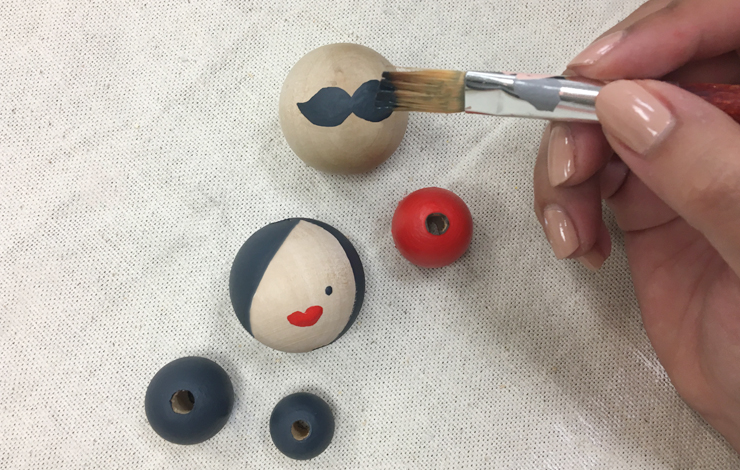 Person painting faces onto the small wood balls.