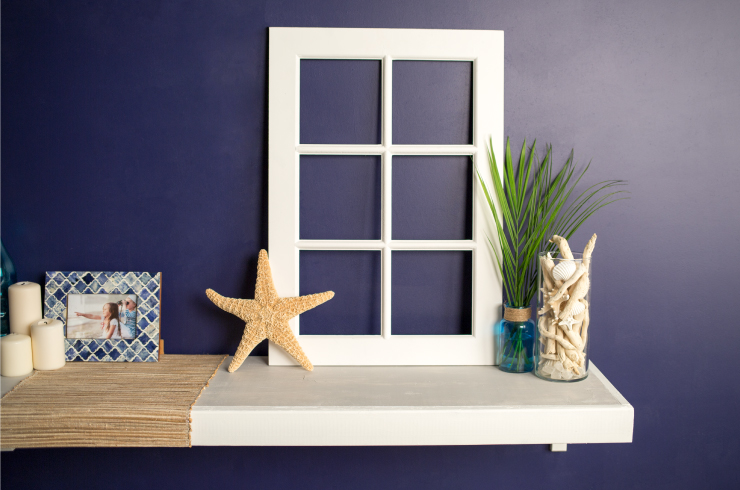 A wall painted in a deep purplish-blue color, Bon Nuit. On the wall is a white shelf decorated with beach décor.