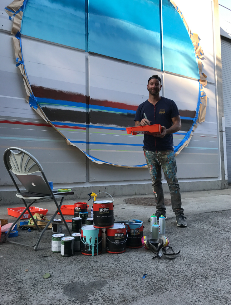 An artist posing in front of his mural that he is painting.