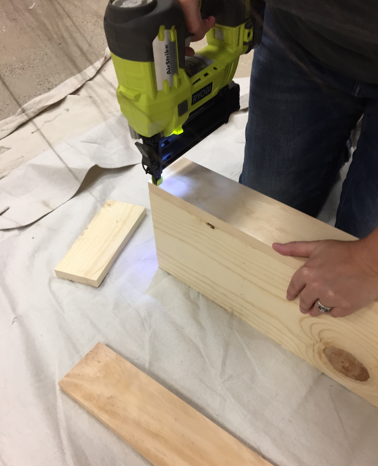 A person with a nail gun assembling the wood pieces to create the box.