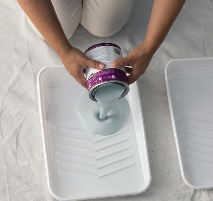 A person pouring light blue paint on a plastic tray liner. 