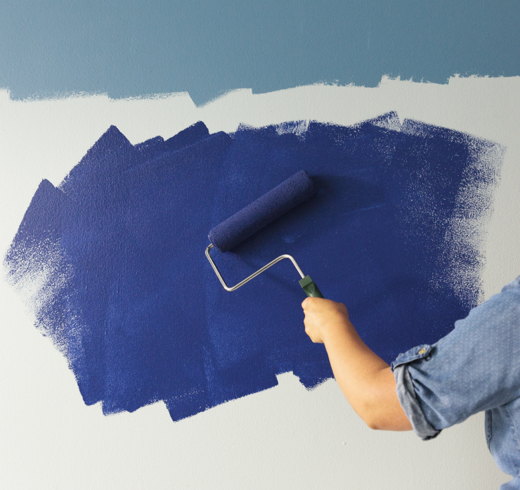 A person painting over the lower wall with a dark blue color. 