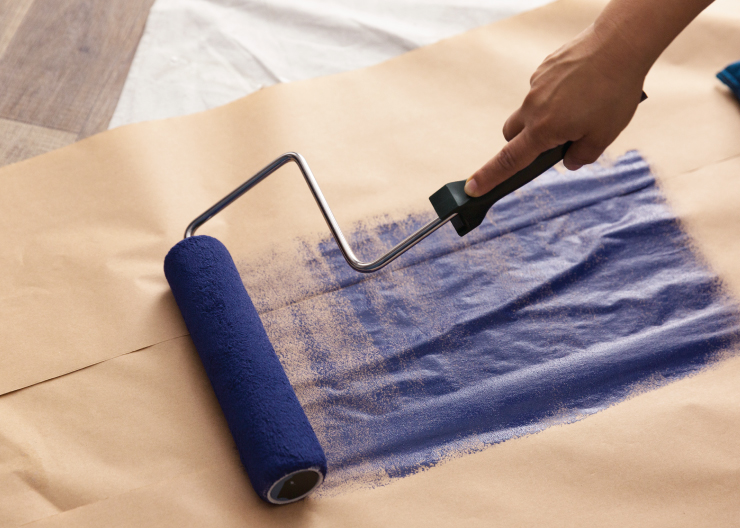 A wet roller with a dark blue color being rolled over paper to get rid of excess paint before beginning wall paint blending process. 