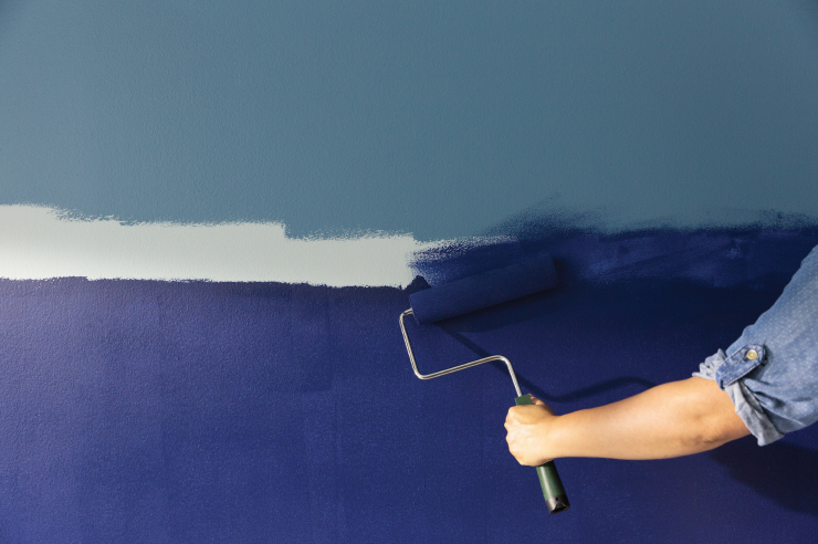 A handheld paint roller starting the paint blending process on a wall painted with three different blue paint colors.