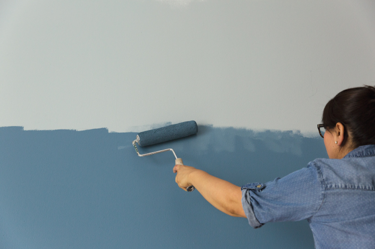 A person paint blending two different blue colors on the wall to create ombre effect. 