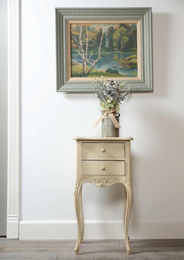 A hallway showing a table with flowers placed on top of it. Above that, on the wall is a large picture. The frame of the picture was painted using Behr’s decorative chalk paint.