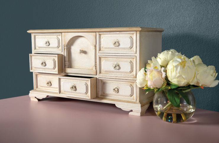 A jewelry box that is painted with Behr decorative chalk paint. The jewelry box is sitting on a table with a vase filled with flowers sitting next to it.