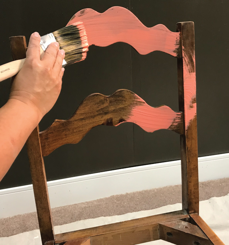 A wooden chair being painted with a salmon color paint color. 