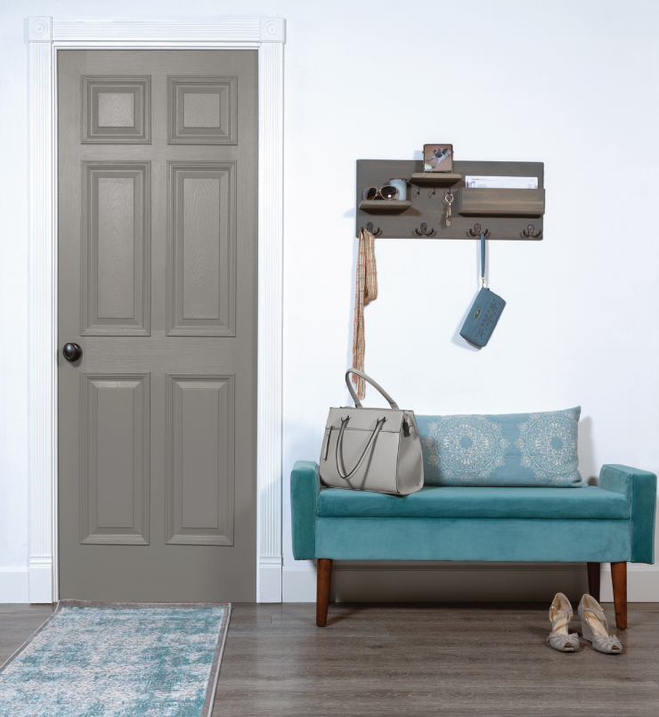 Entryway with a blue velvet bench propped with a white and blue pillow. Purse is on bench, shows on floor. Above the bench is a wood shelf with hooks for scarfs, wallets, sunglasses and keys. The walls are white. The door is painted in Elephant Skin. In front of the door is a rug colored in blue and white.