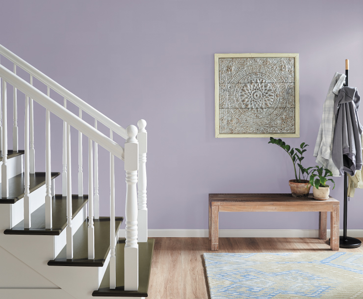 A light purple hallway and staircase area with minimal decorative elements. Hallway decorative elements include a sitting bench, coat rack. and wall artwork. 