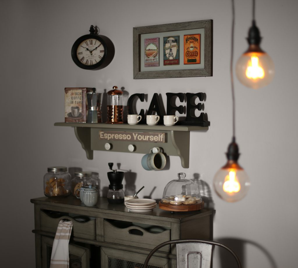 A close up of the buffet cabinet displaying coffee items; mugs, grinder, café sign. The hanging lights are blurred in the foreground of the image.