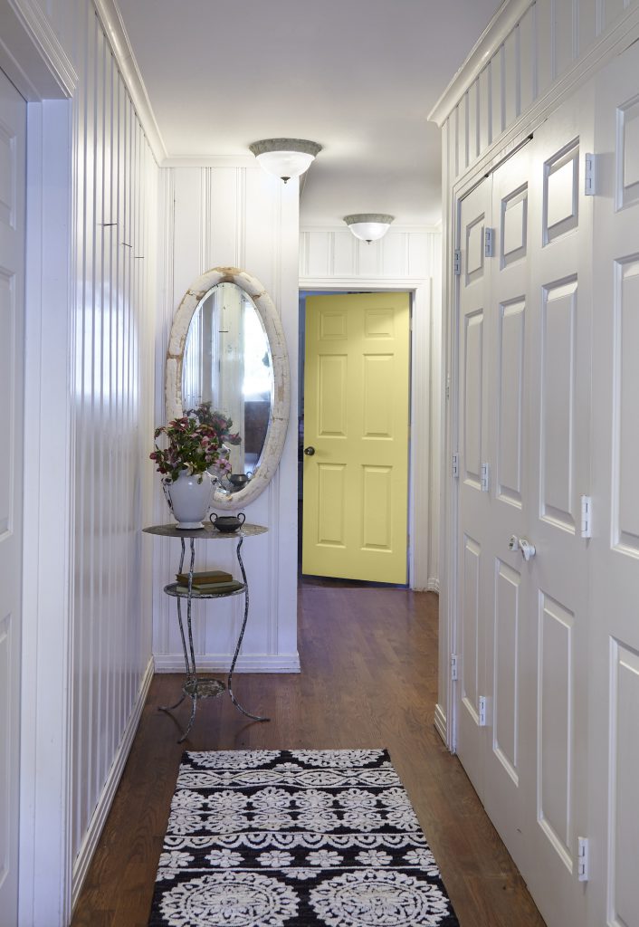 A hallway with white walls. The door at the end is painted in a bright yellow color, Spring Grass.
