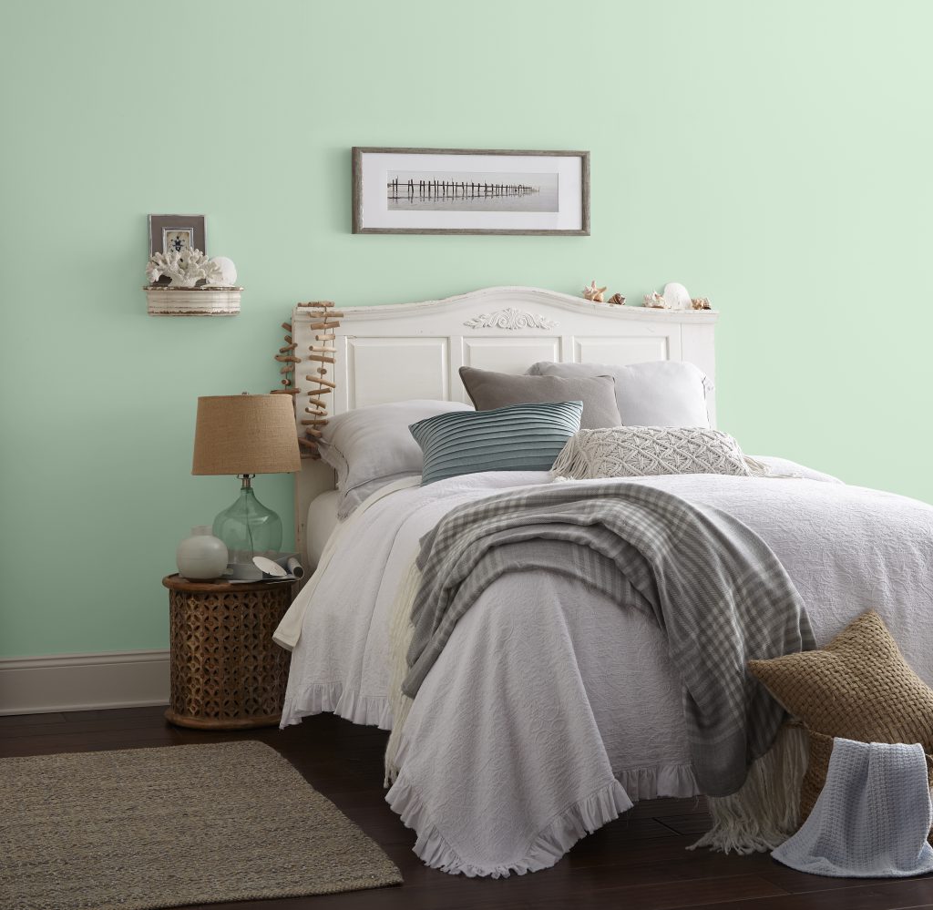 A peaceful coastal style bedroom with light green wall and comfy white bed. 