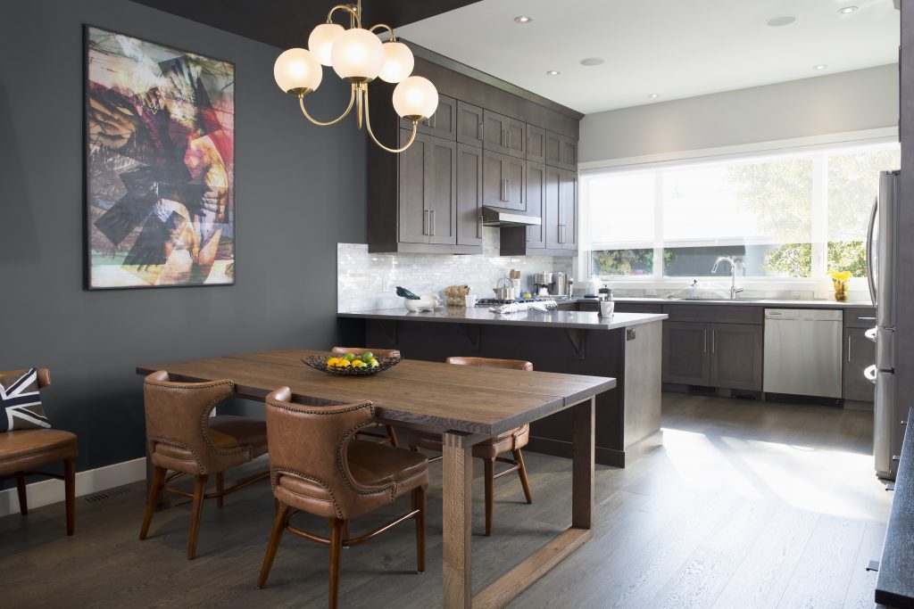 An open floor plan featuring a kitchen and dining area, painted in Graphic Charcoal.  A kitchen with plenty of cabinet storage. A dining area with warm toned wood and leather furniture. 