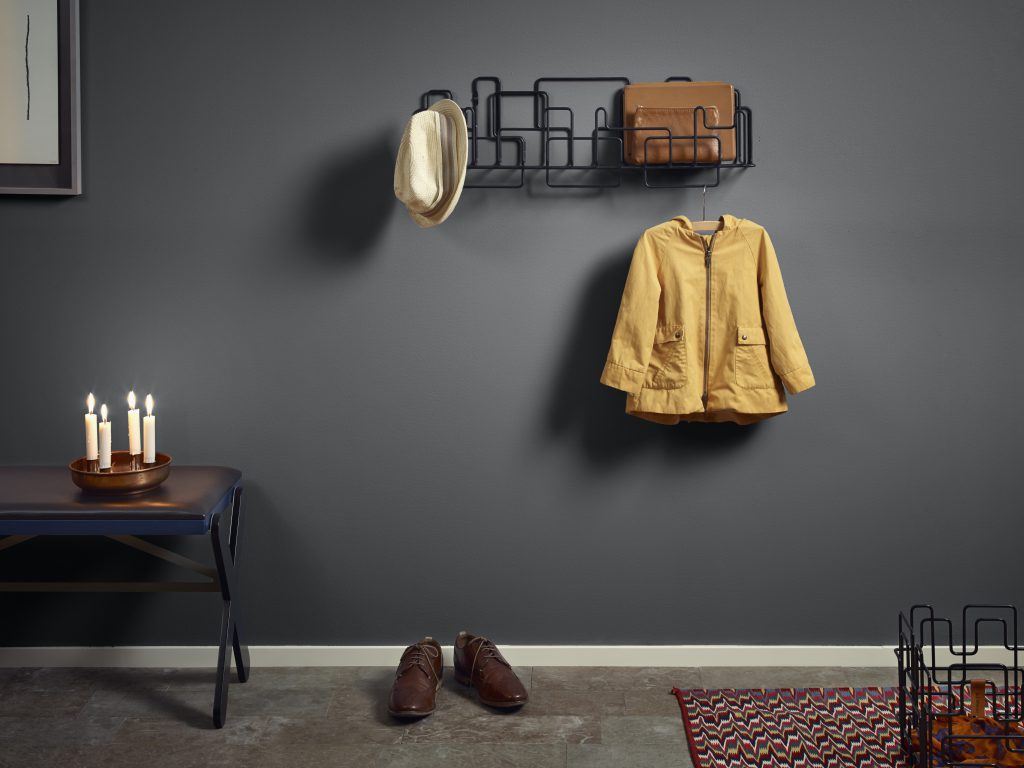 A modern hallway painted in a gray color called Graphic Charcoal. A metal coat rack shaped in an artistic wall statement. Several warm toned furniture and decorative elements. 