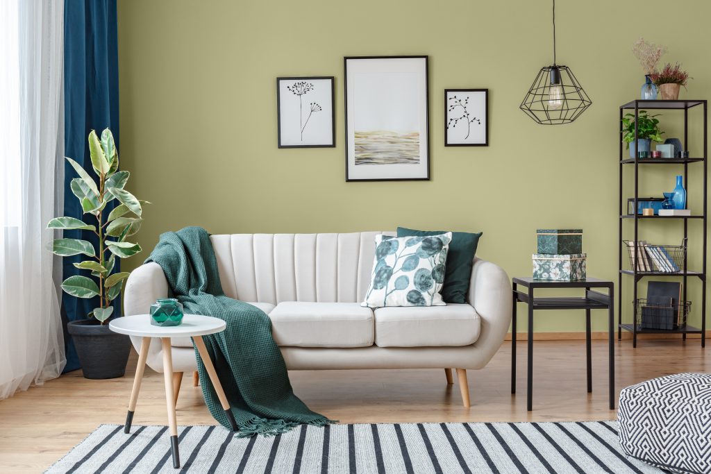 A modern living room painted in green color called Secret Meadow.  A mix of neutral and dark green furniture and decor items. 