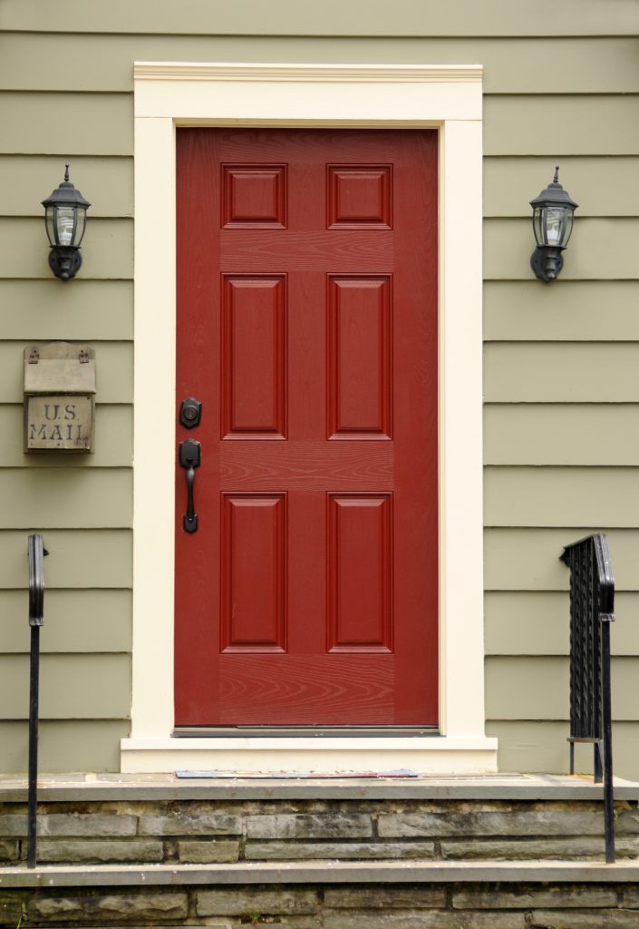 A siding home exterior featuring a main front door painted in a red color called Red Pepper. Metal mailbox mounted on siding wall, wrought iron railings and lamps 