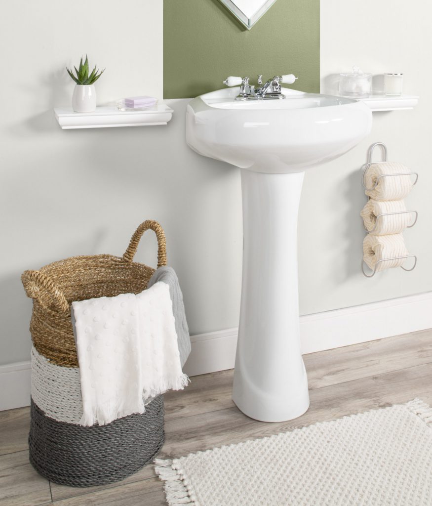 A low view of bathroom showing decorative items: basket holding towels, plant on shelf, toilet paper holder showing rolls wrapped in organic decorative paper.