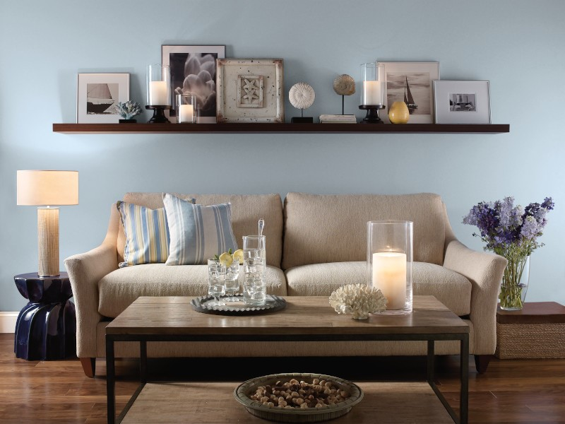 This living room area has a beige sofa on the center.  The decor is nautical with blue and  natural sand colors. The room featured dark hardwood floor. 