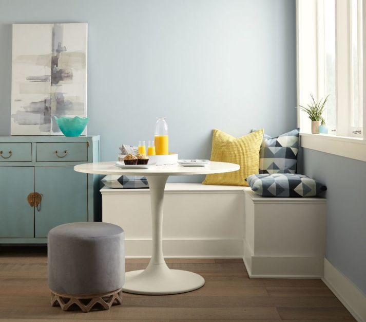 A breakfast nook decorated with casual and modern furniture.  The walls are painted in light color called Light Drizzle. The overall room is accented by a pop of yellow and teal. 