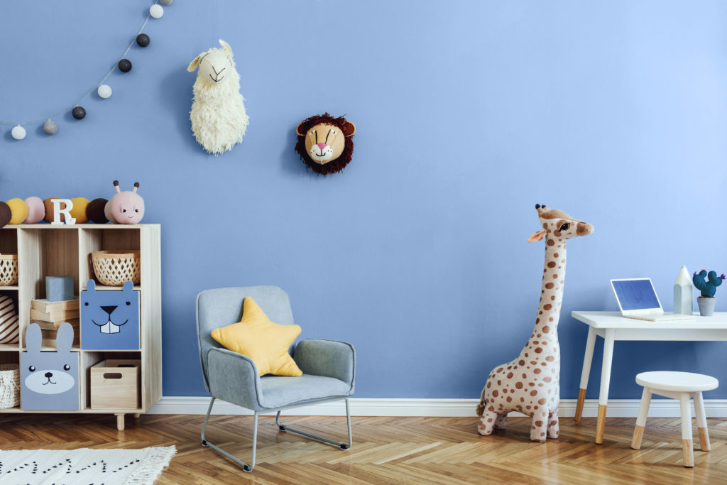 A blue Scandinavian nursery-playroom with wooden cabinet, desk, mint color armchair, baby accessories and toys.