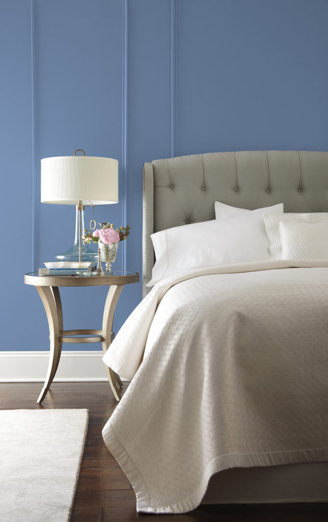 A chic blue bedroom with light gray upholstered bed headboard and dark hardwood floor which creates a sense of serenity and balance.