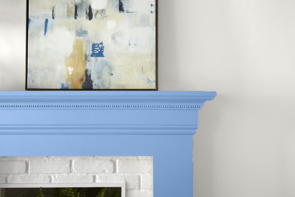 A wood fireplace mantel painted an unexpected blue color called Bluebird and an abstract painting sitting on top of the mantle and leaning on white wall.