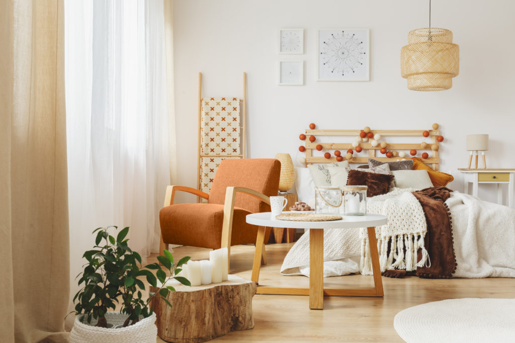 A cozy bedroom interior with comfortable orange chair facing the windows standing next to a wooden small table.