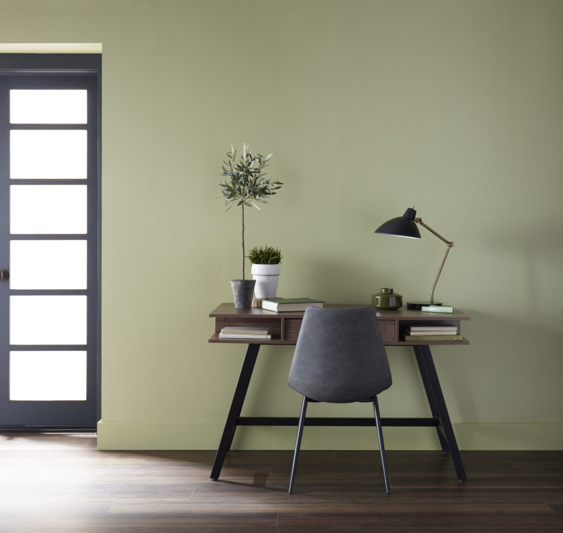 A home office with a small desk sitting against a green painted wall.