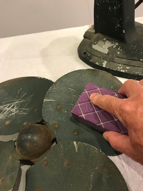 A man's hand sanding the old paint from the old cooling fan blades. 