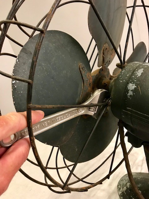 A man's hand removing the fan guard using a small adjustable wrench.