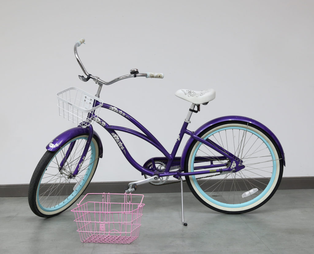 An old purple colored bike with white flowers.
