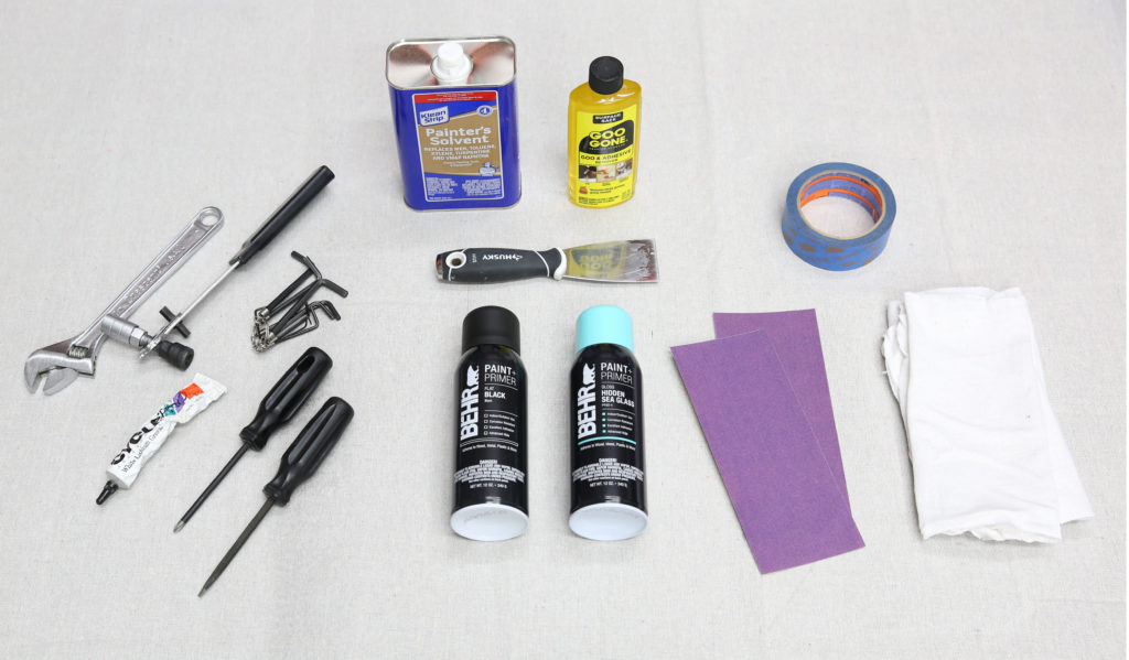 A drop cloth with tools placed on it. The tools are from the list below showing what is needed to spray paint a bike.
