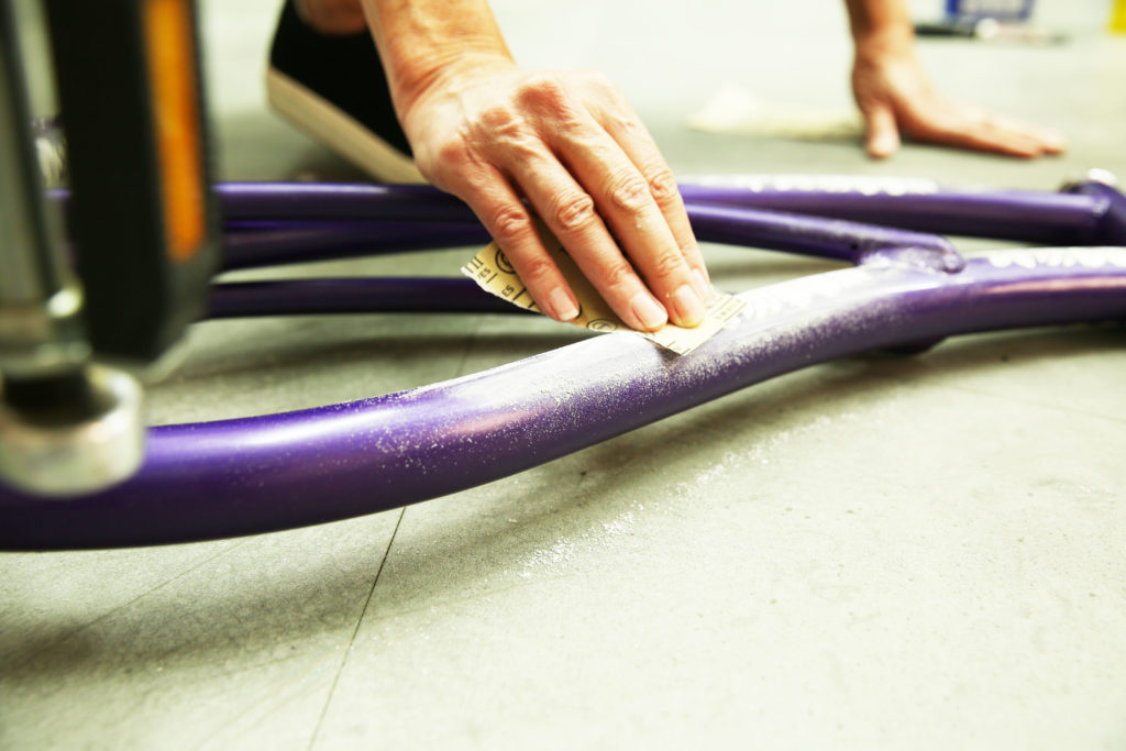 A person using a sheet of sandpaper on the bike.