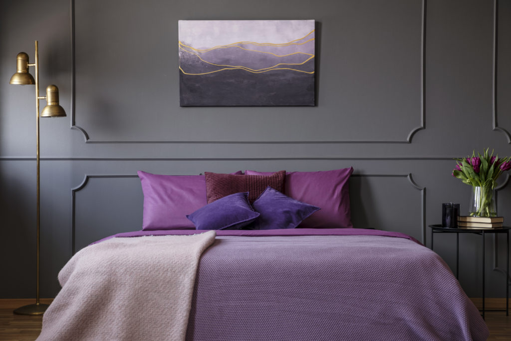 An elegant bedroom with painting on the wall and a big bed in the center, the bed is dressed in this striking magenta hue which adds  dramatic impact to the space.   

