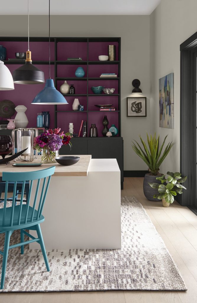 A eclectic dining area featuring a fireplace and bookshelf built-in, a magenta background color creates a dramatic backdrop for displaying eclectic décor pieces.