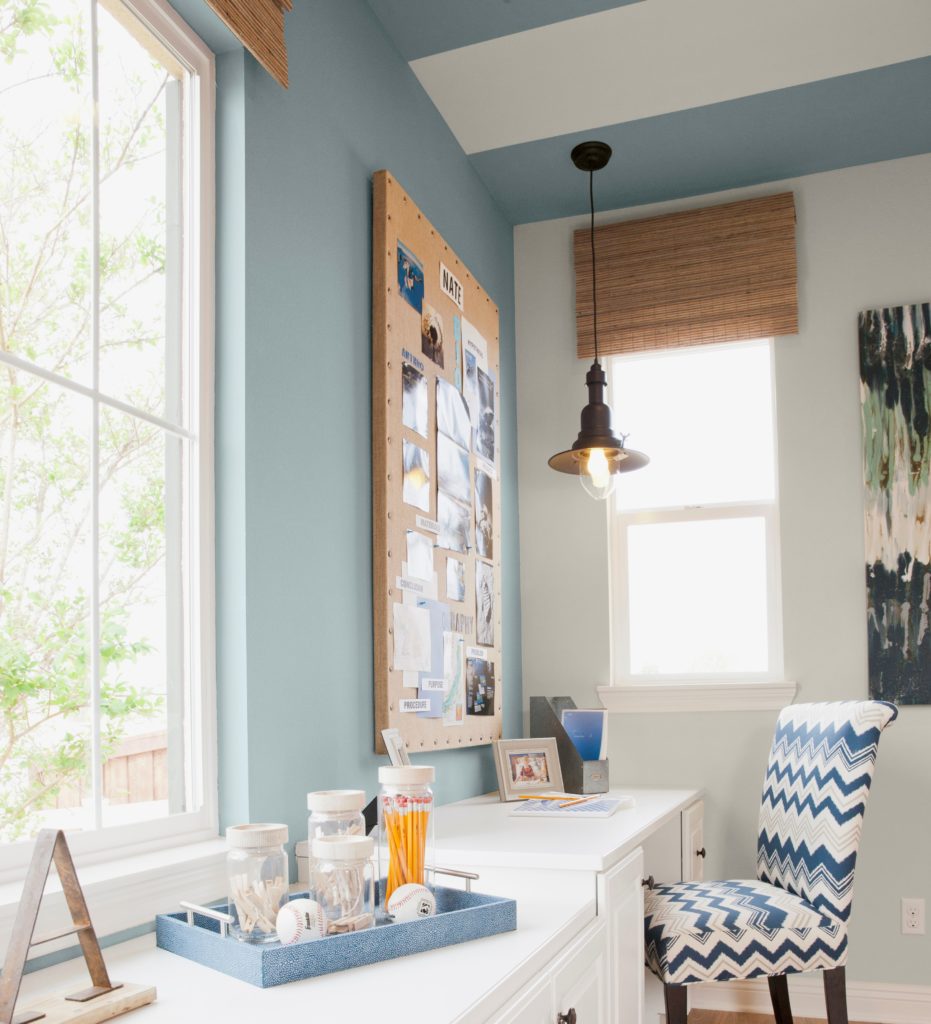 A small and  narrow shaped study with two windows, a desk with white cabinets.  A small wall area painted with a blue color called Dayflower.