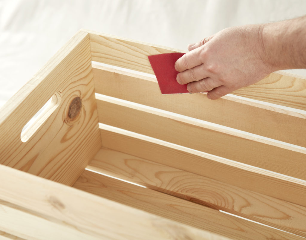 A person using sandpaper against the wooden crate.