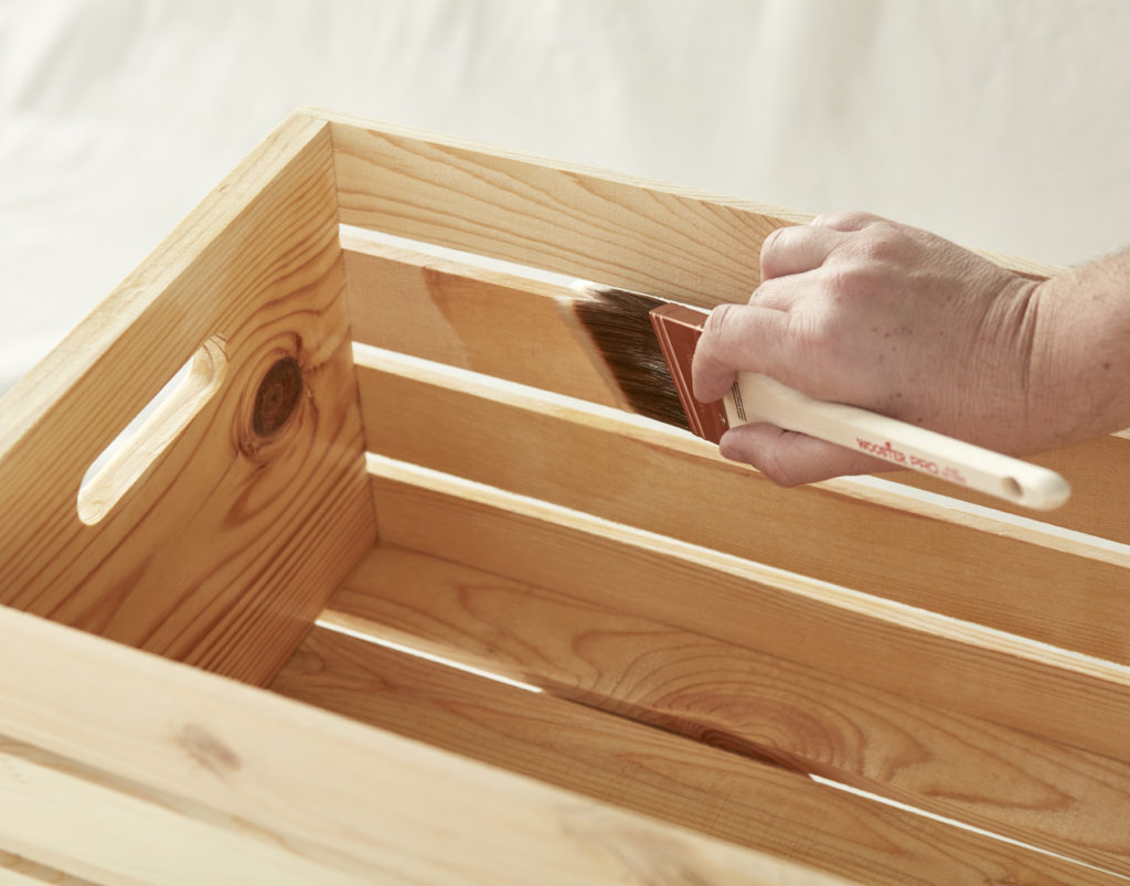 A person holding a paint brush again the wooden crate