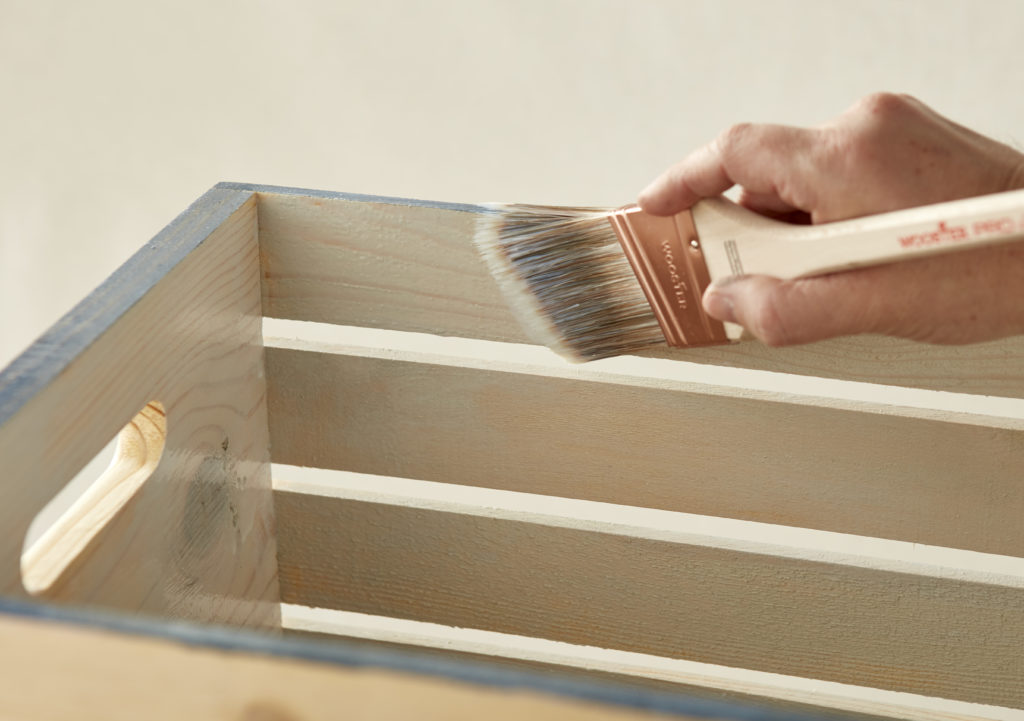A person holding a paint brush against a wooden crate.