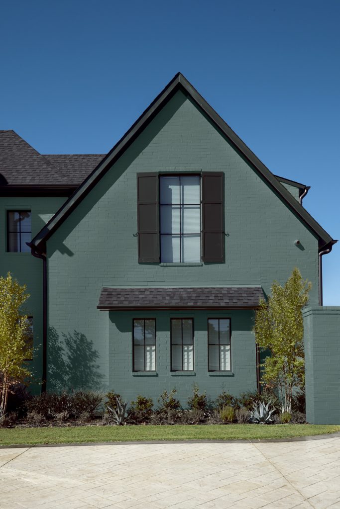A dark green two-story brick house with dark brown shutters. 