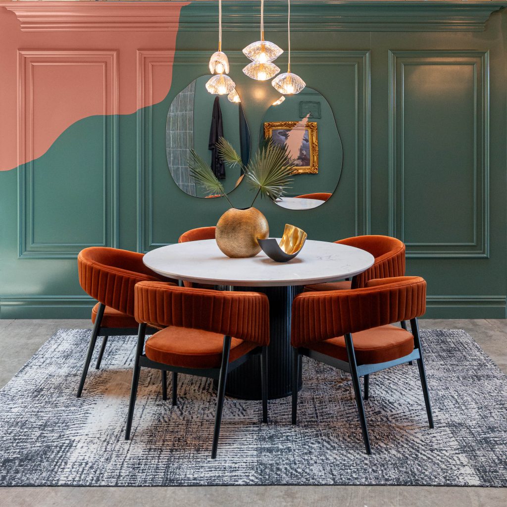 A dining room with plush chairs. The walls are painted in a deep Jade Hue with a splash of a bold orange popping in on the side.