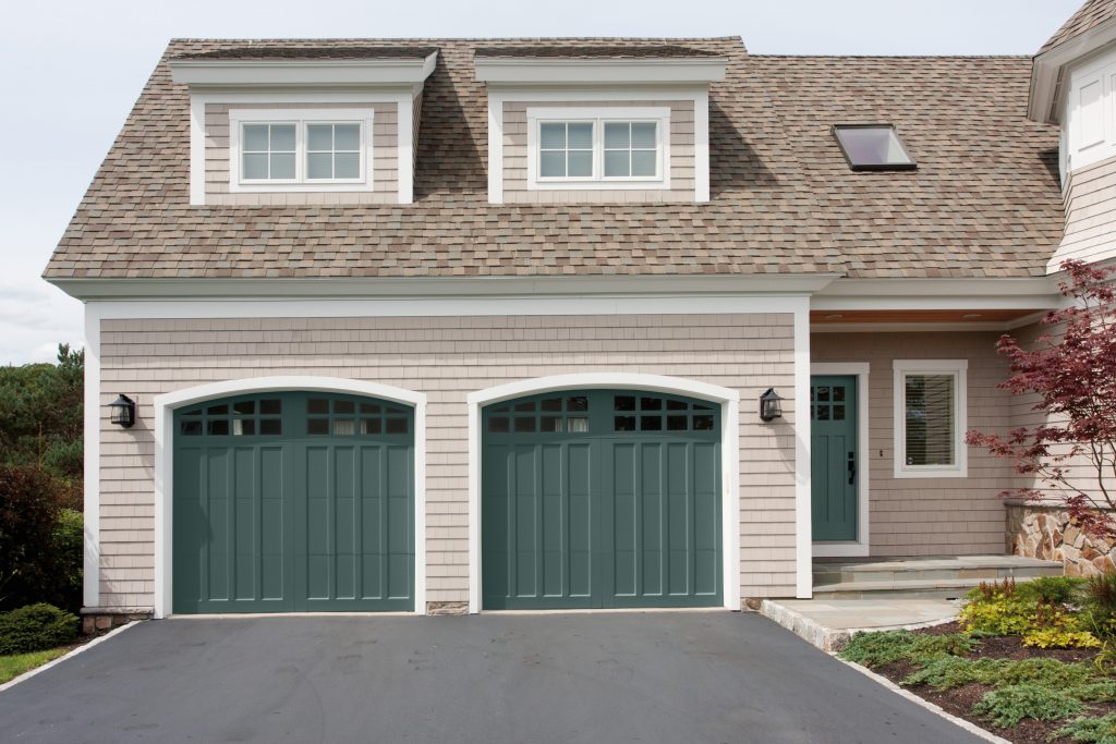 A house with pink-beige siding, dark green double garage, dormer windows, and landscaped front yard.