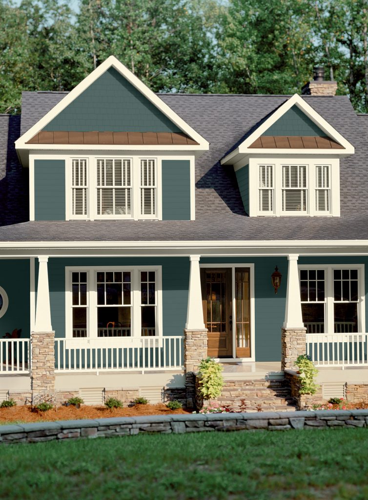 A green two-story house with white trim, stone accents and natural wood front door.  