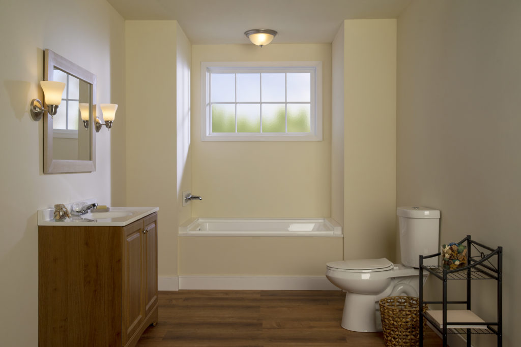 A not very exciting looking bathroom, the color of the wall is beige, the sink is made with a natural wood color and the hardware and lighting fixtures are very generic and bland looking. 