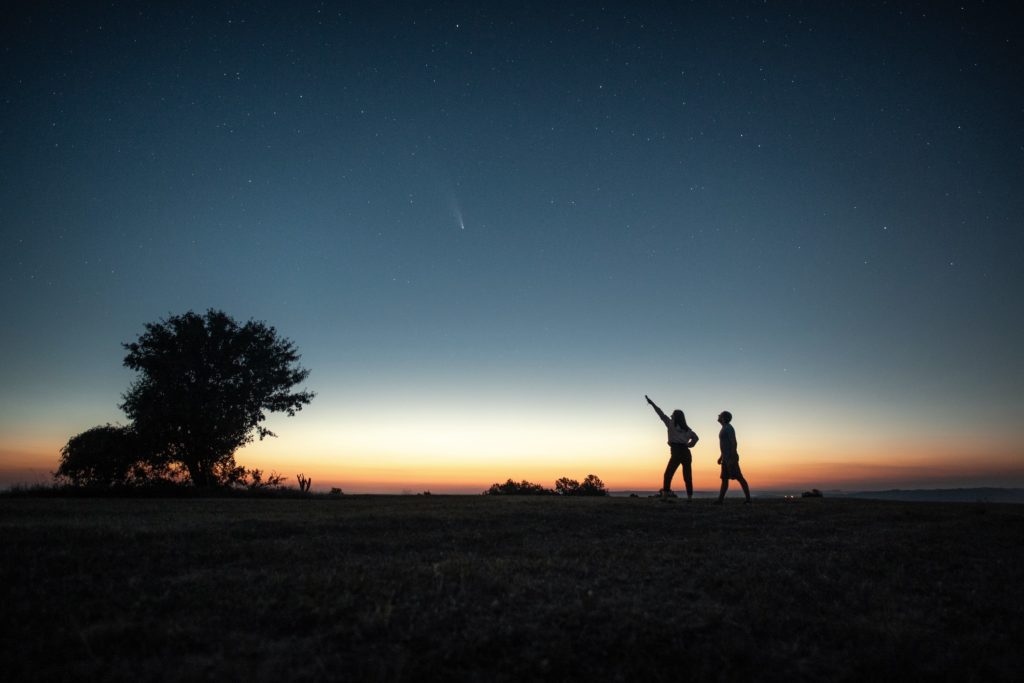 Silhouette of a young couple watching the Neowise comet  under the bright blue night sky after sunset.