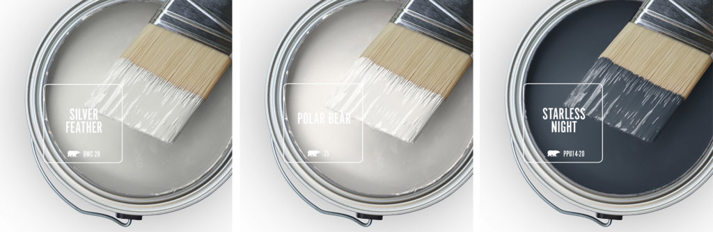 Three open paint cans with a half dipped brushes.  There is a light warm gray color, a white and a dark, almost black navy blue. 