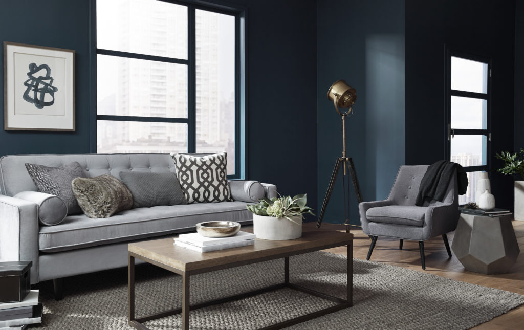A moody, modern Livingroom area with gray upholstered sofa and accent chair.  The decorating style looks masculine. The walls are painted in a dark blue color called Nocturne Blue. 